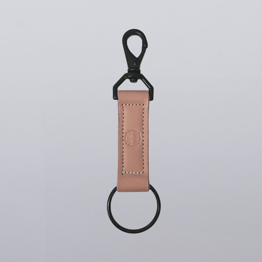 The Handy-Dandy Keychain by Hanks Belts is a handmade pink leather keychain with black stitching, a black metal clip with snap at the top, and a round black key ring at the bottom, shown on a light gray background.