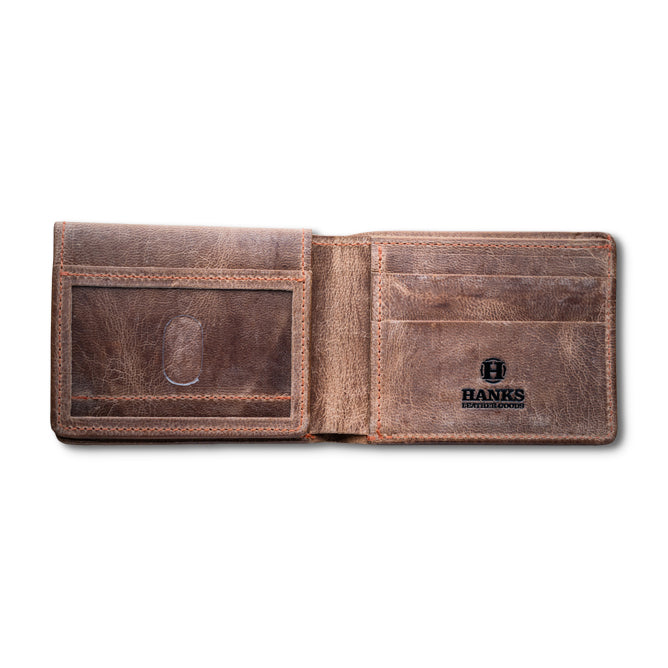 The Huron Premium Bifold with ID Window by Hanks Belts is a brown steerhide wallet, made in the USA, featuring card slots, a clear ID window, and an interior "Hanks" logo. The distressed leather adds a rustic, vintage touch.