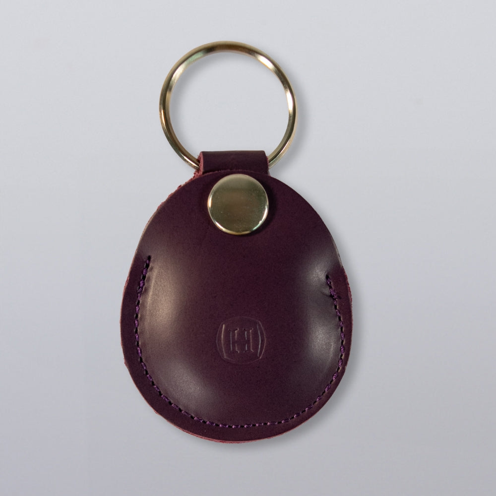Hanks Belts’ Circular Tag Holder is a round, purple full-grain leather keychain with a gold metal ring and snap button, embossed initials on the front, and shown on a plain light gray background—both stylish and durable.
