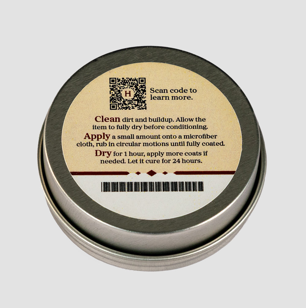 A round metal tin of Hanks Belts Leather Conditioning Balm features a label with care instructions, a QR code, and bolded words "Clean," "Apply," and "Dry" to guide you in maintaining CCW belts or belt dressing.