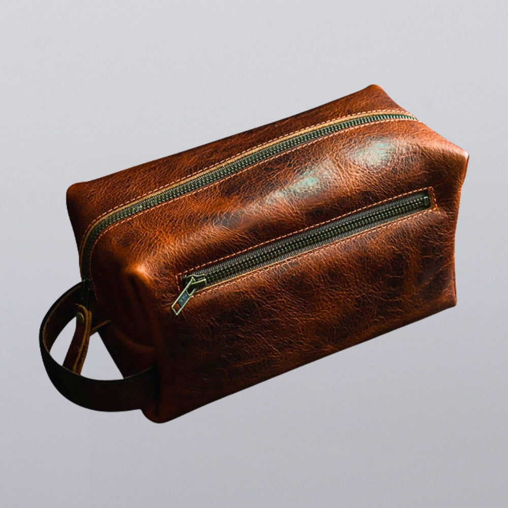 The Hanks Belts Bison Deluxe Leather Dopp Bag With Zipper, made in the USA, features brown Bison leather, a handle, and two zippered compartments. Displayed against a plain light gray background.