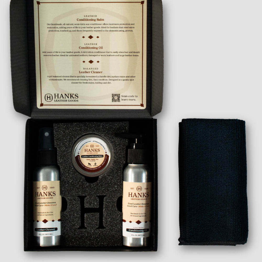 An open Hanks Belts Leather Preserve Kit box contains two bottles of cleaner and conditioner, a small jar, and a black cloth, all neatly arranged in foam. Product instructions appear on the lid.