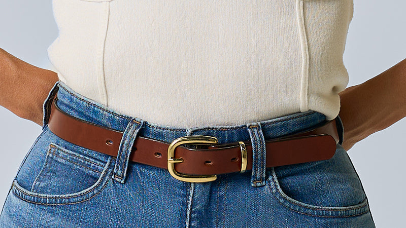 Person wearing a beige top and blue jeans with a brown belt and gold buckle.