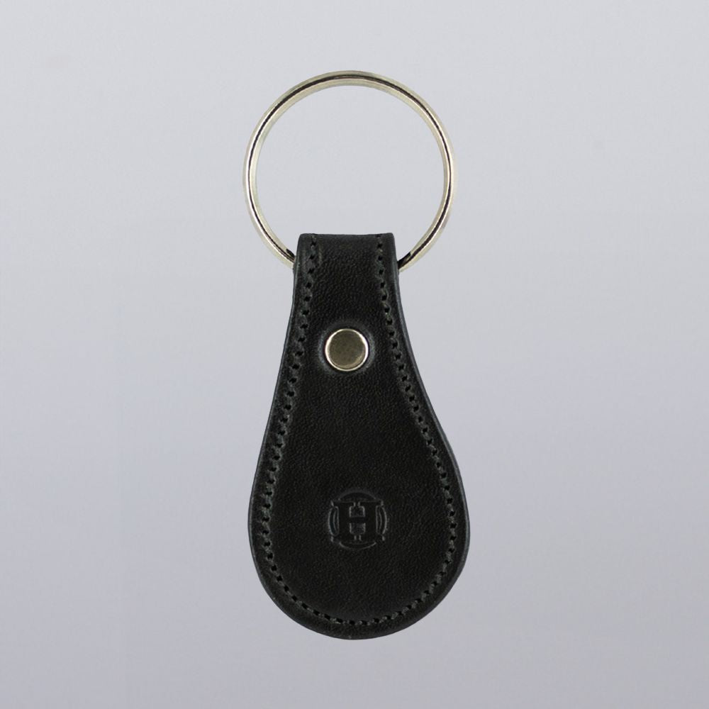The Bell-Shaped Leather Keychain by Hanks Belts features full grain leather, a teardrop silhouette, metal ring, detailed edge stitching, and an embossed logo at the bottom center. Made in the USA.