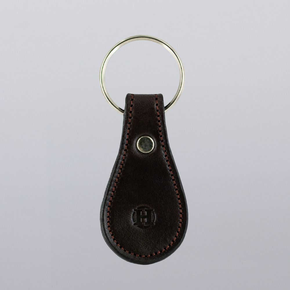 The Hanks Belts Bell-Shaped Leather Keychain features full grain dark brown leather with red stitching, a metal snap button, and a round keyring, shown on a plain light gray background.