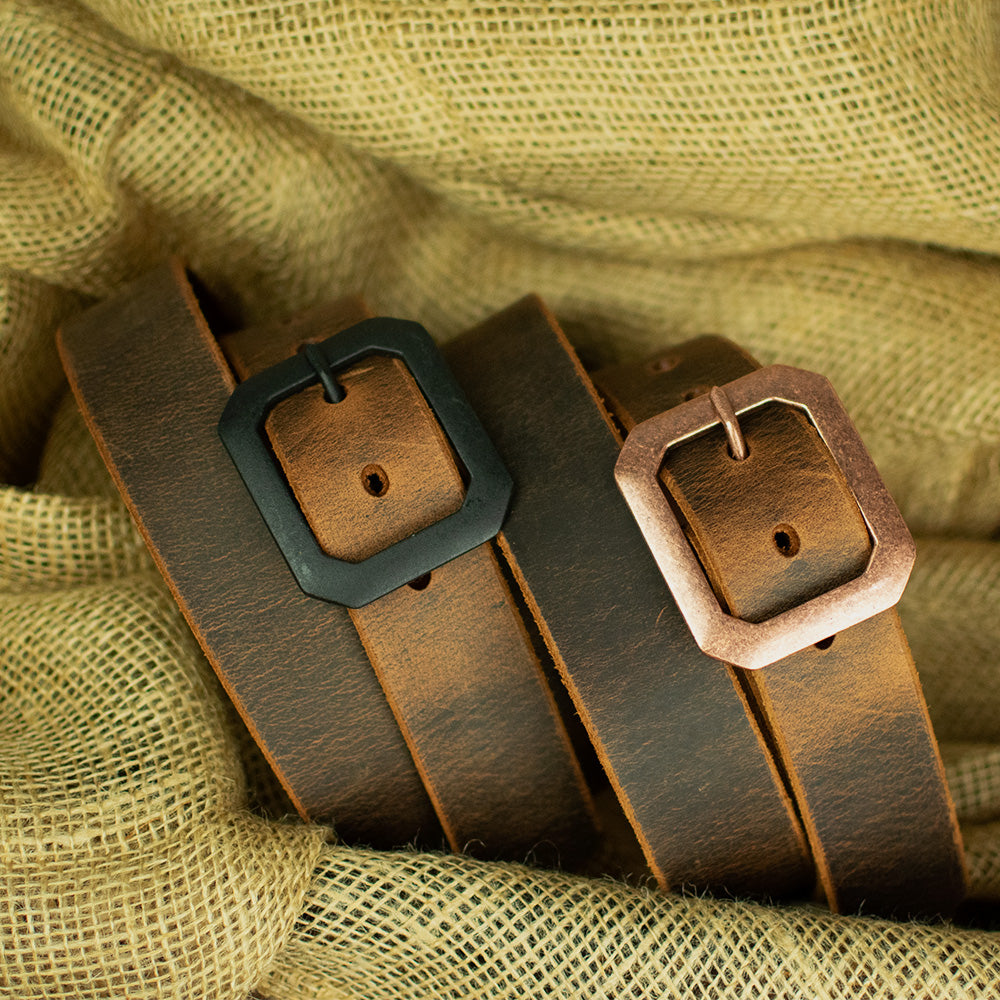 Two Hanks Belts "The Relic Retro Style" Water Buffalo leather belts, one with a black square buckle and one with a bronze square buckle, are displayed side by side on textured burlap fabric.