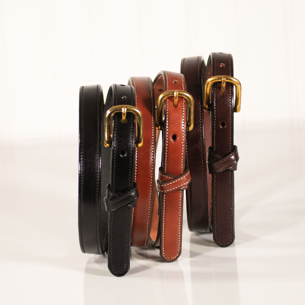 Four Hanks Belts "The Dixie" women’s belts crafted from premium English Bridle leather in black, tan, and brown, each with a gold buckle, stand upright on a white surface, highlighting quality American craftsmanship.