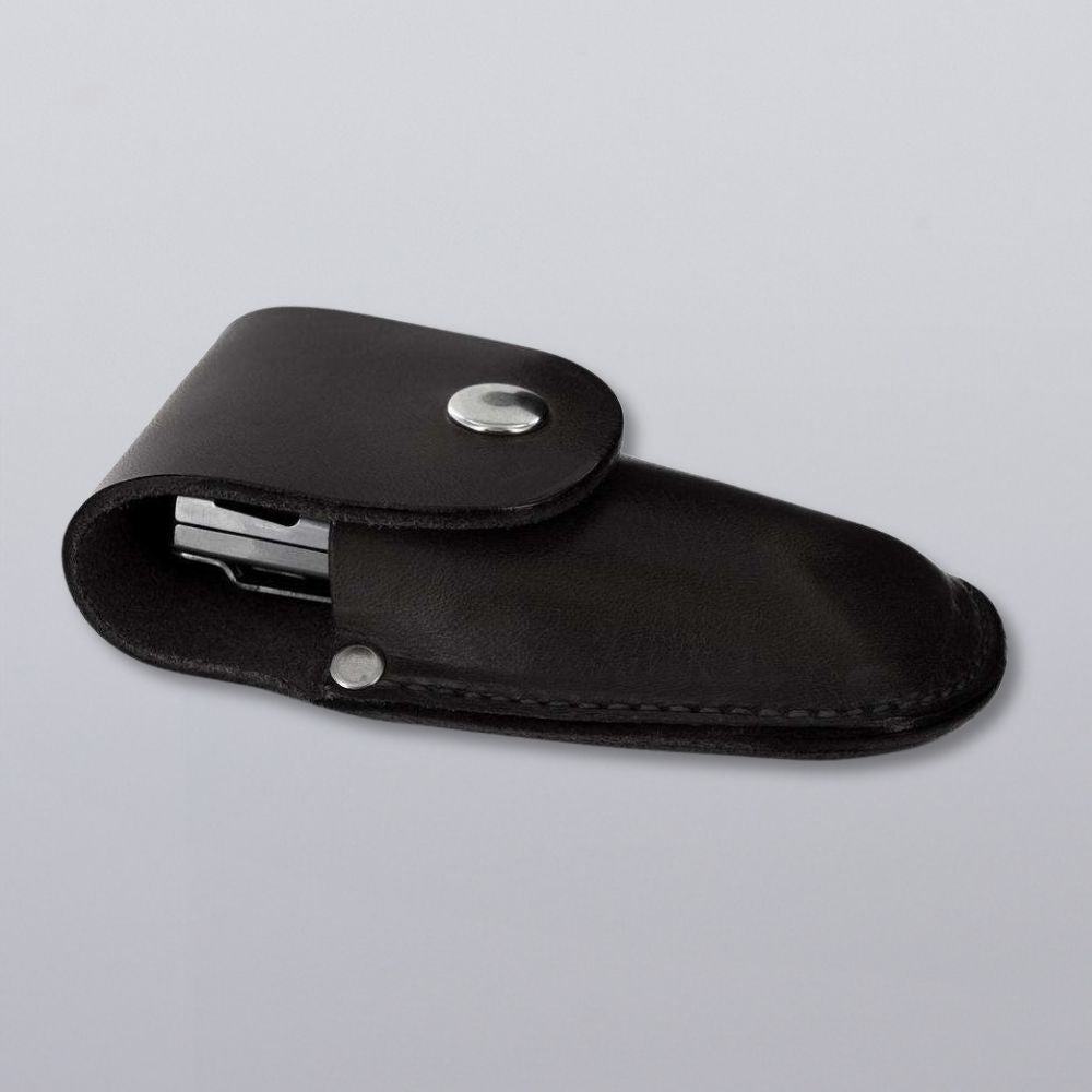 The Canyon Utility Sheath and Mag Case by Hanks Belts, crafted from black bridle leather with a silver snap flap, holds a partially visible metal object and is shown on a plain light gray surface.