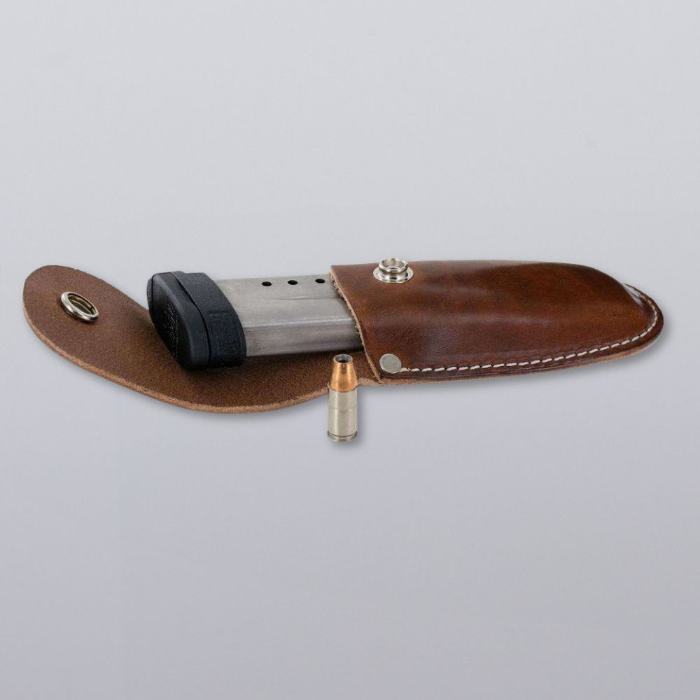 The Canyon Utility Sheath and Mag Case by Hanks Belts, made of handcrafted bridle leather with a snap closure, holds a metal handgun magazine and one round of ammunition, shown against a plain light gray background.