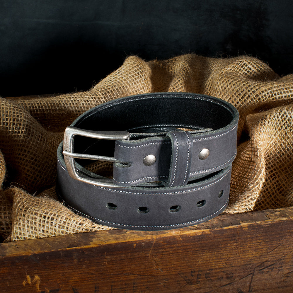 The Suede Belt - 1.5" by Hanks Belts, made in the USA, is coiled on burlap. The rustic wooden backdrop contrasts beautifully with the suede's sleek texture and silver buckle.