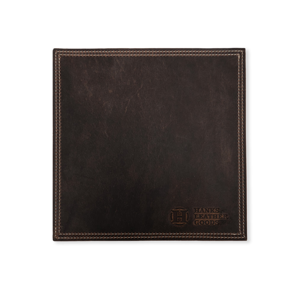 This square leather mouse pad is crafted from North American Bison leather and features visible stitching along the edges. In the bottom right corner, you'll find an embossed logo that reads "Hanks Belts." This premium desk accessory boasts a smooth, dark brown finish and is part of the Desk & Mouse Pad Set.