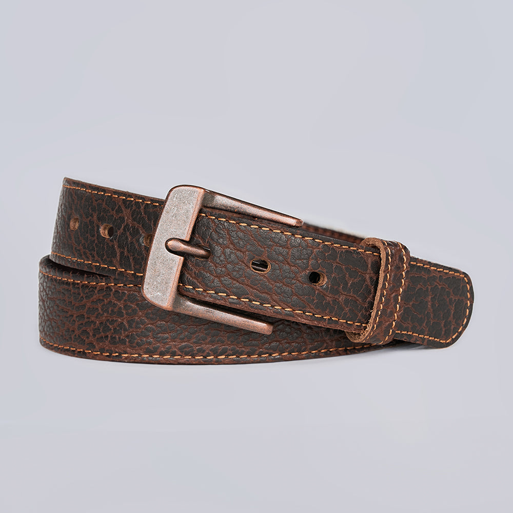 The Yellowstone by Hanks Belts is a rugged shrunken brown leather belt with a textured pattern, light brown edge stitching, and a silver metal buckle, shown against a plain light grey background.