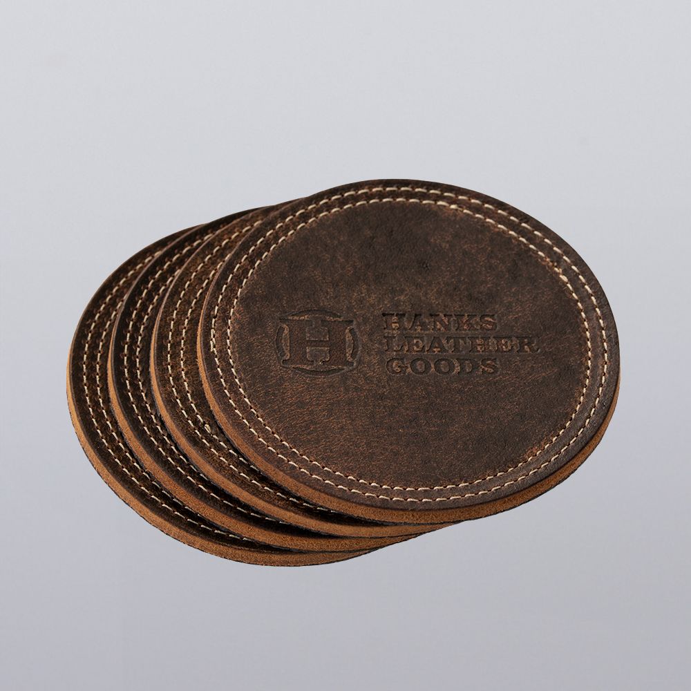 A stack of Premium Round Leather Coasters - Set of 4 by Hanks Belts, featuring visible stitching and an embossed logo on the top coaster, displayed against a plain light background.