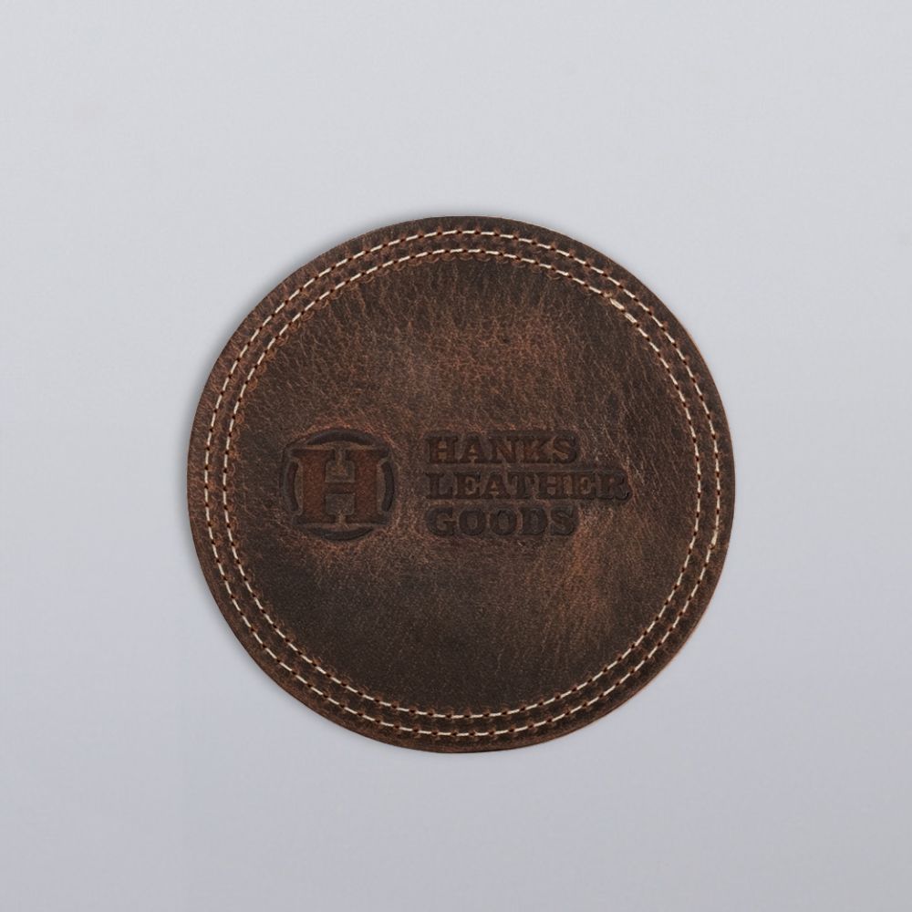 The Premium Round Leather Coasters - Set of 4 by Hanks Belts feature brown bison leather, visible edge stitching, and "HANKS LEATHER GOODS" embossed in the center—an ideal gift-ready addition for any occasion.
