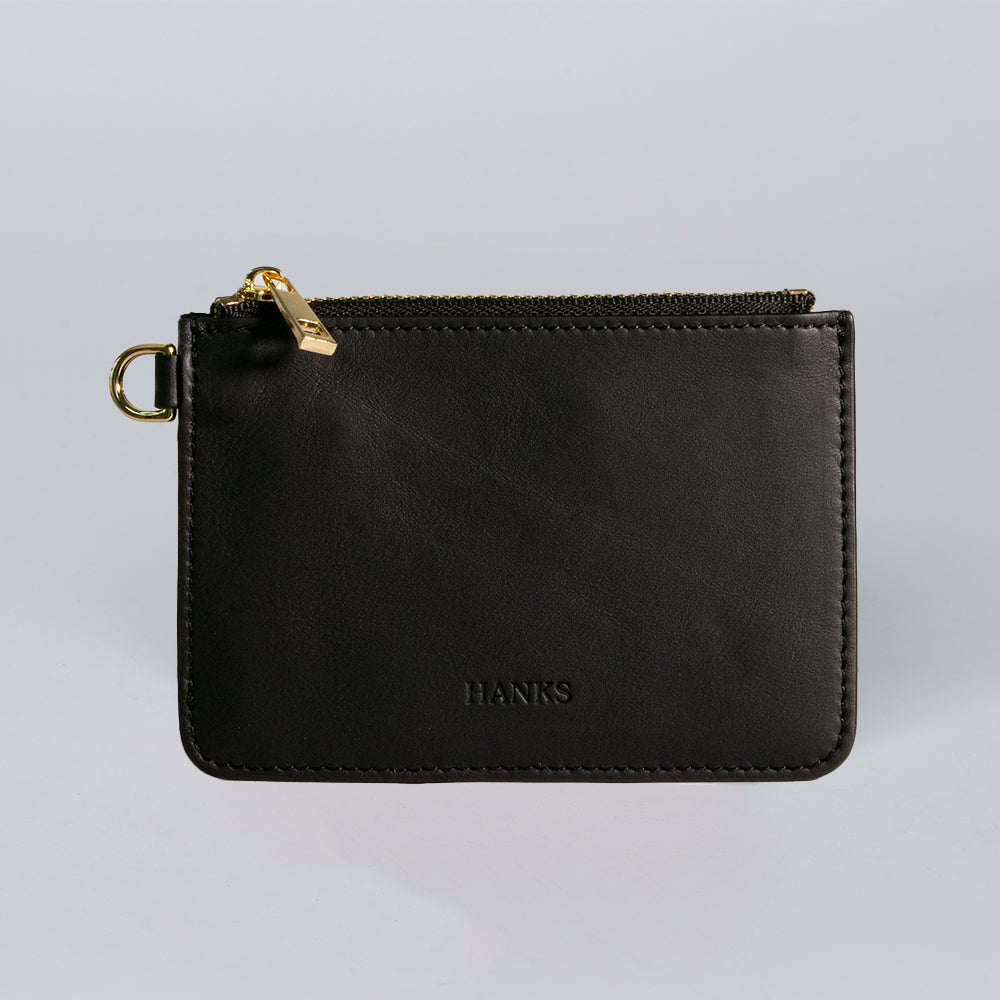 The Livia Mini Wristlet by Hanks Belts is a black Italian leather wallet with a gold zipper and small gold ring, displayed on a plain light gray background.