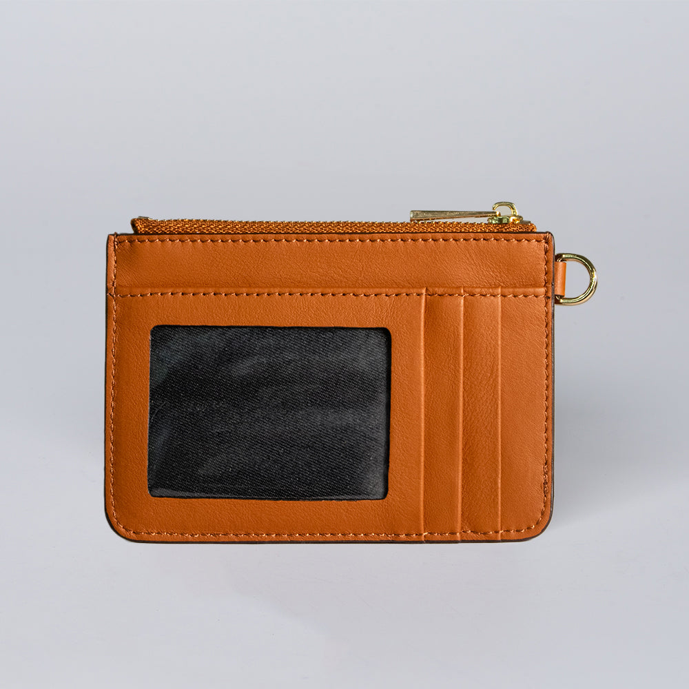 The Hanks Belts Livia Mini Wristlet is a small brown leather cardholder with a clear ID window, three card slots, a top zip compartment, and a gold key ring, displayed on a plain light gray background.
