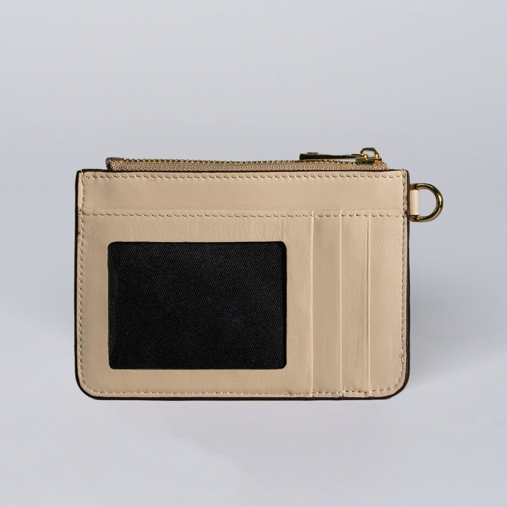 The Hanks Belts Livia Mini Wristlet, shown against a plain light background, features beige leather, a transparent ID window, three card slots, a zippered compartment, and a small gold ring on the side.