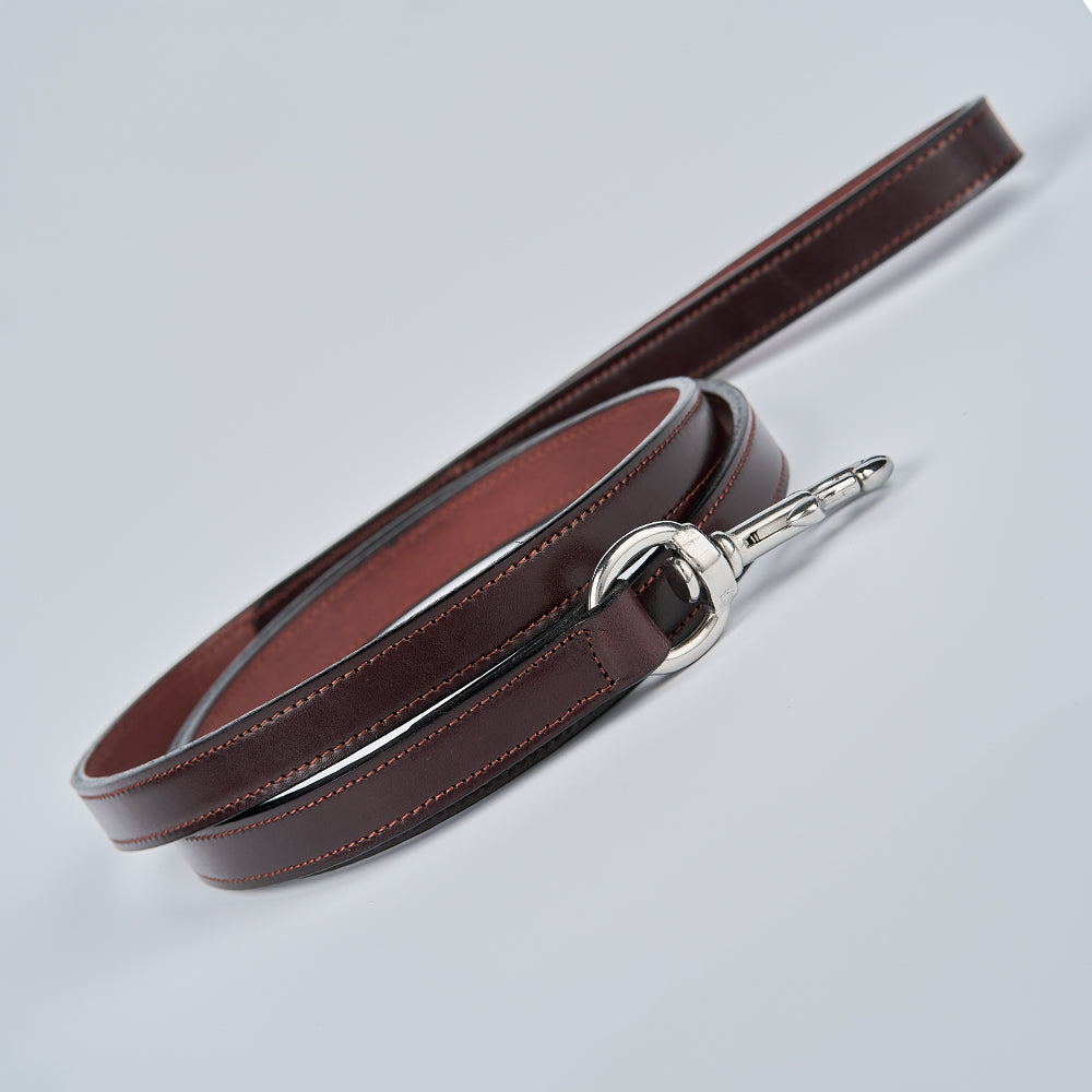The Hanks Belts Old Reliable Leash, made in the USA from brown English bridle leather with visible stitching and a shiny silver clasp, is shown coiled neatly against a plain light background.