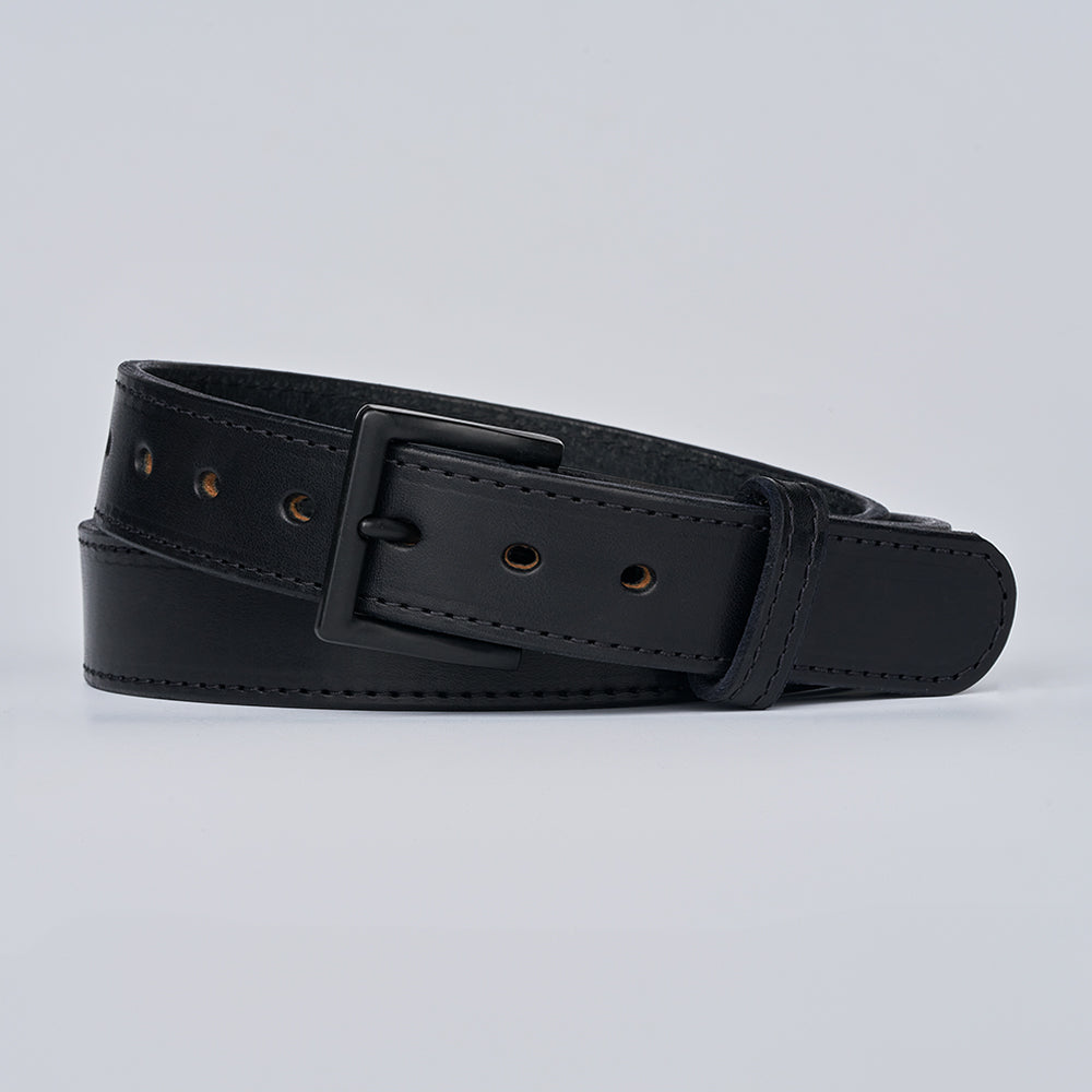 The Black Out Tactical by Hanks Belts is a black leather CCW belt with a matte black rectangular buckle, evenly spaced holes, and visible edge stitching, rolled up on a light gray background.