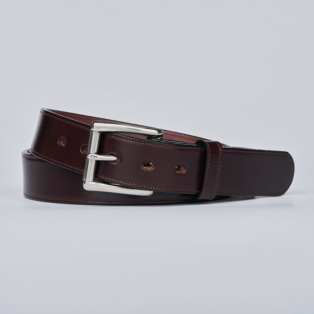The Canyon by Hanks Belts is a dark brown English bridle leather belt with a silver rectangular buckle, handcrafted and neatly coiled on a plain light gray background.