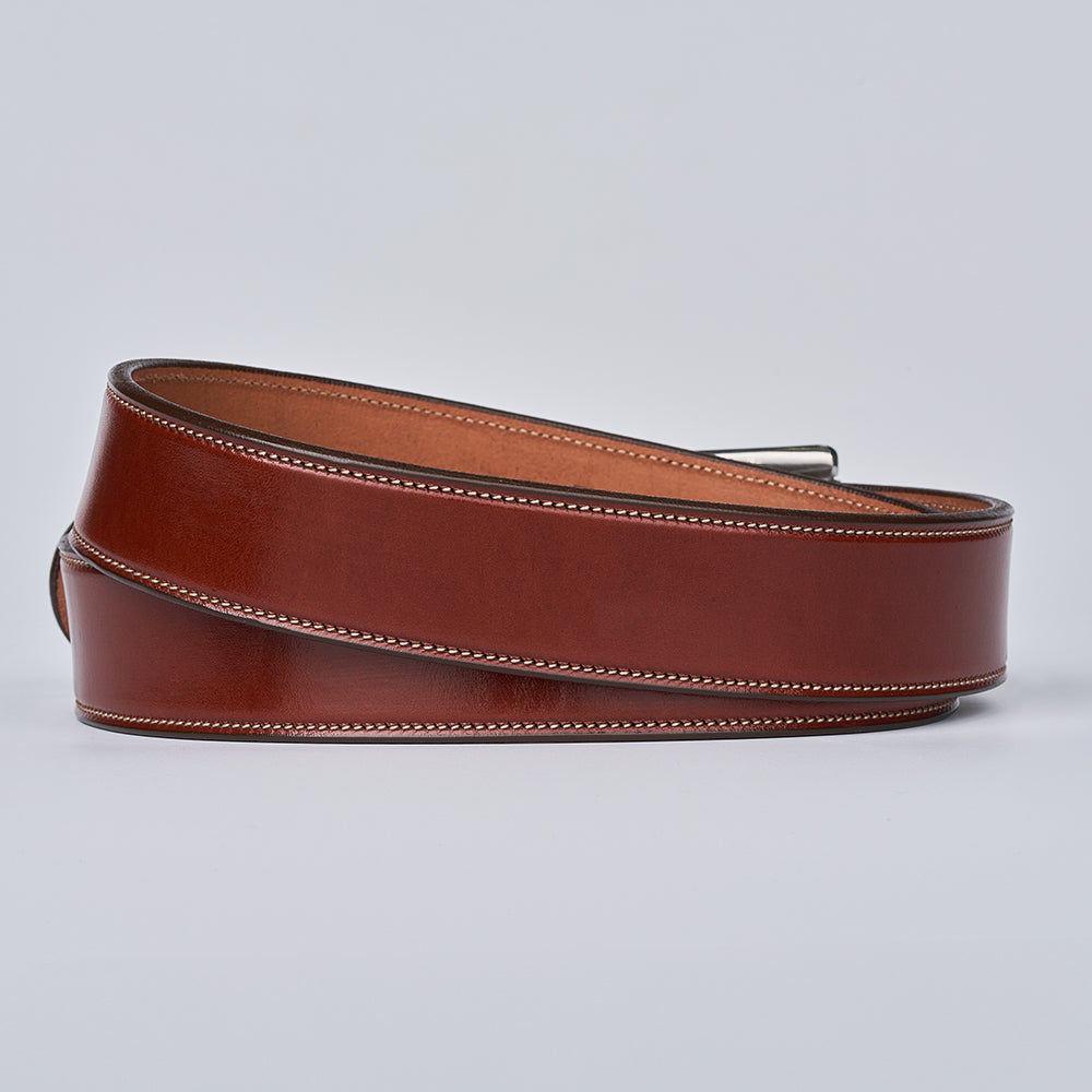 The Canyon belt by Hanks Belts, crafted from English bridle leather with white edge stitching, is shown coiled in a loose loop on a plain light gray background.