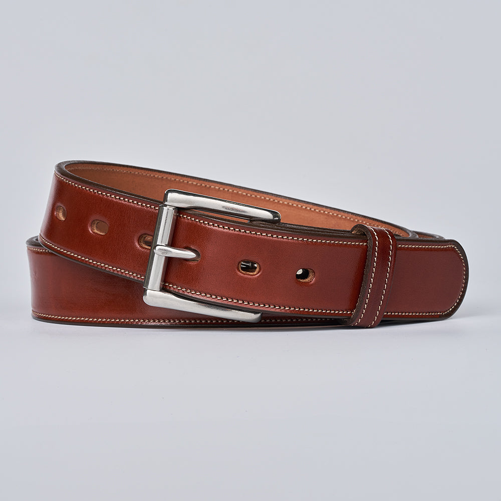 The Canyon by Hanks Belts is a handcrafted English bridle leather belt with white stitching, a silver rectangular buckle, and multiple holes, shown coiled on a light gray background.
