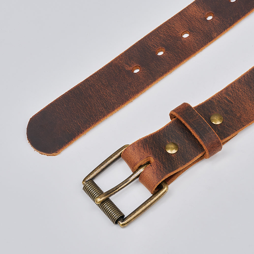 A close-up of The Crazy Horse by Hanks Belts, a retro leather belt with a brass buckle and multiple adjustment holes, crafted from premium Water Buffalo leather and shown on a light gray background.