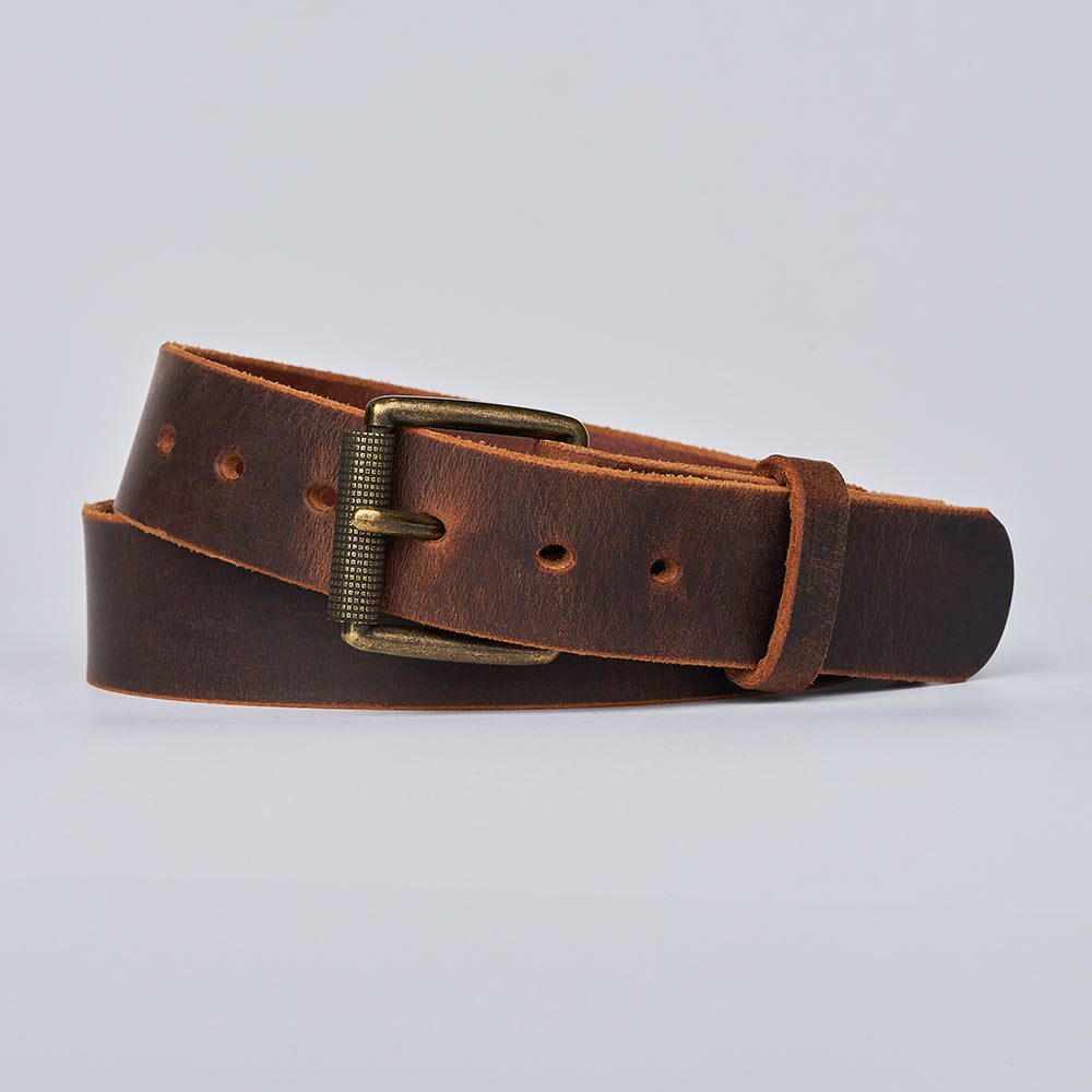 The Crazy Horse by Hanks Belts, crafted from brown Water Buffalo leather with a brass buckle, is coiled on a light gray background. This retro belt features visible stitching and multiple holes for adjustable sizing.