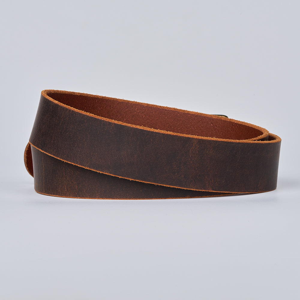 The Crazy Horse belt by Hanks Belts is a coiled strip of dark brown Water Buffalo leather with lighter tan edges, shown on a plain light gray background.