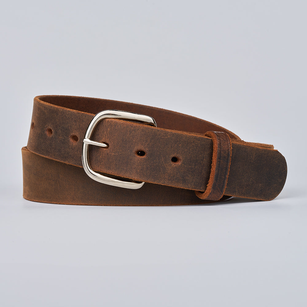 The Crazy Horse by Hanks Belts is a retro brown Water Buffalo leather belt with a silver buckle, multiple holes, and a smooth, slightly worn texture. It’s shown coiled neatly on a plain light gray background.
