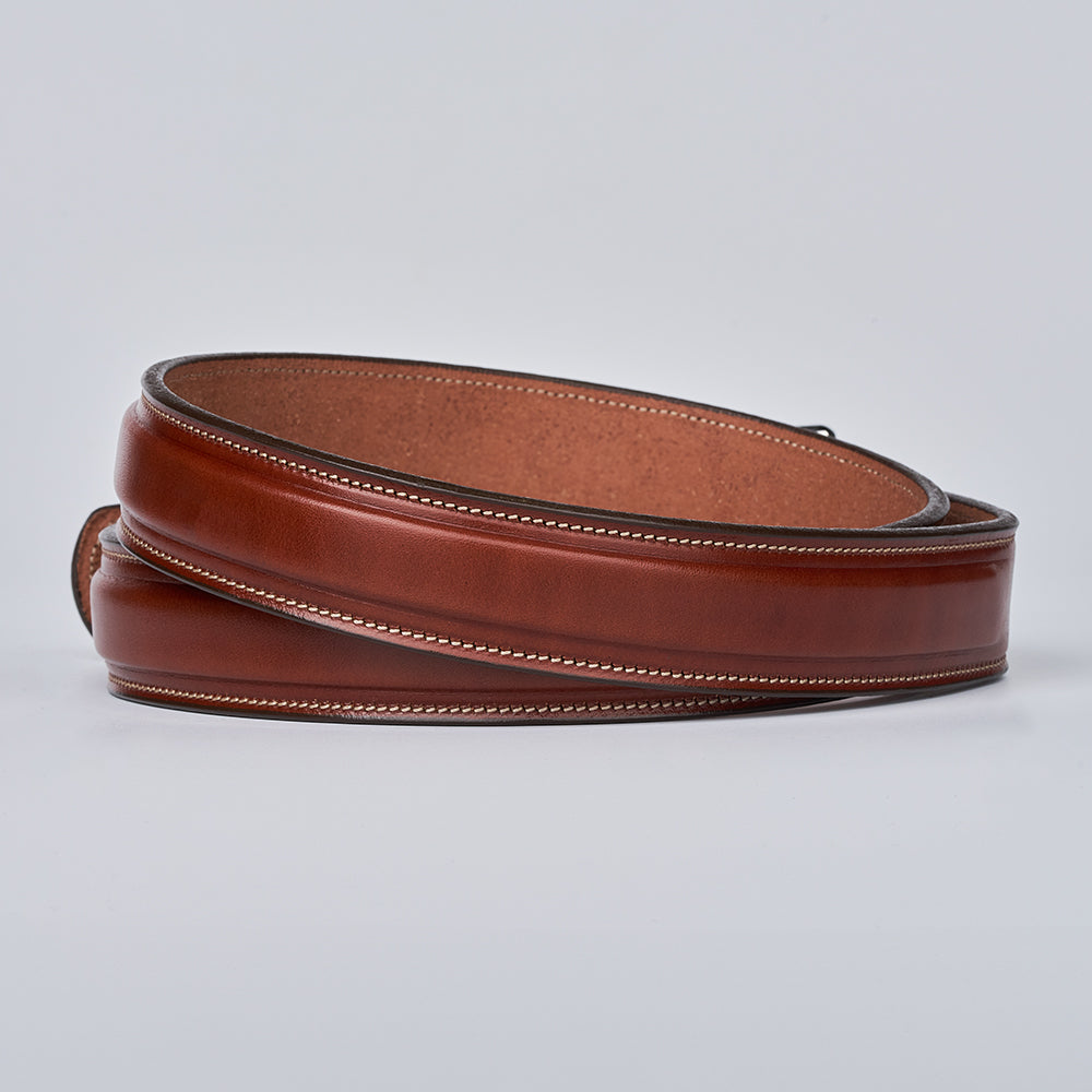 The Esquire Raised belt by Hanks Belts, crafted from brown English Bridle leather with light edge stitching, is shown coiled against a plain light gray background.
