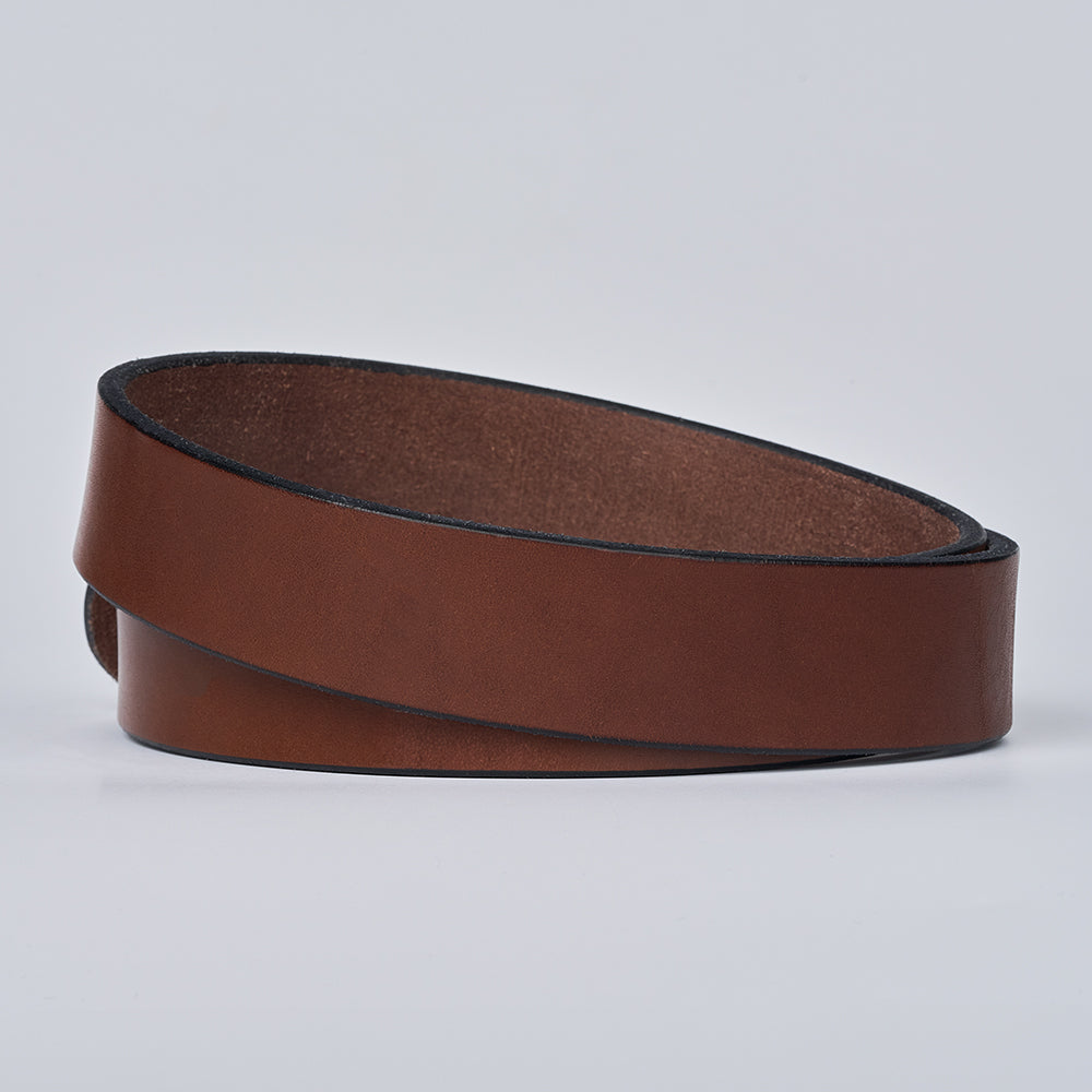 The Everyday belt by Hanks Belts, crafted from brown full grain leather with a black edge, is coiled in a loop and shown on a plain light gray background.
