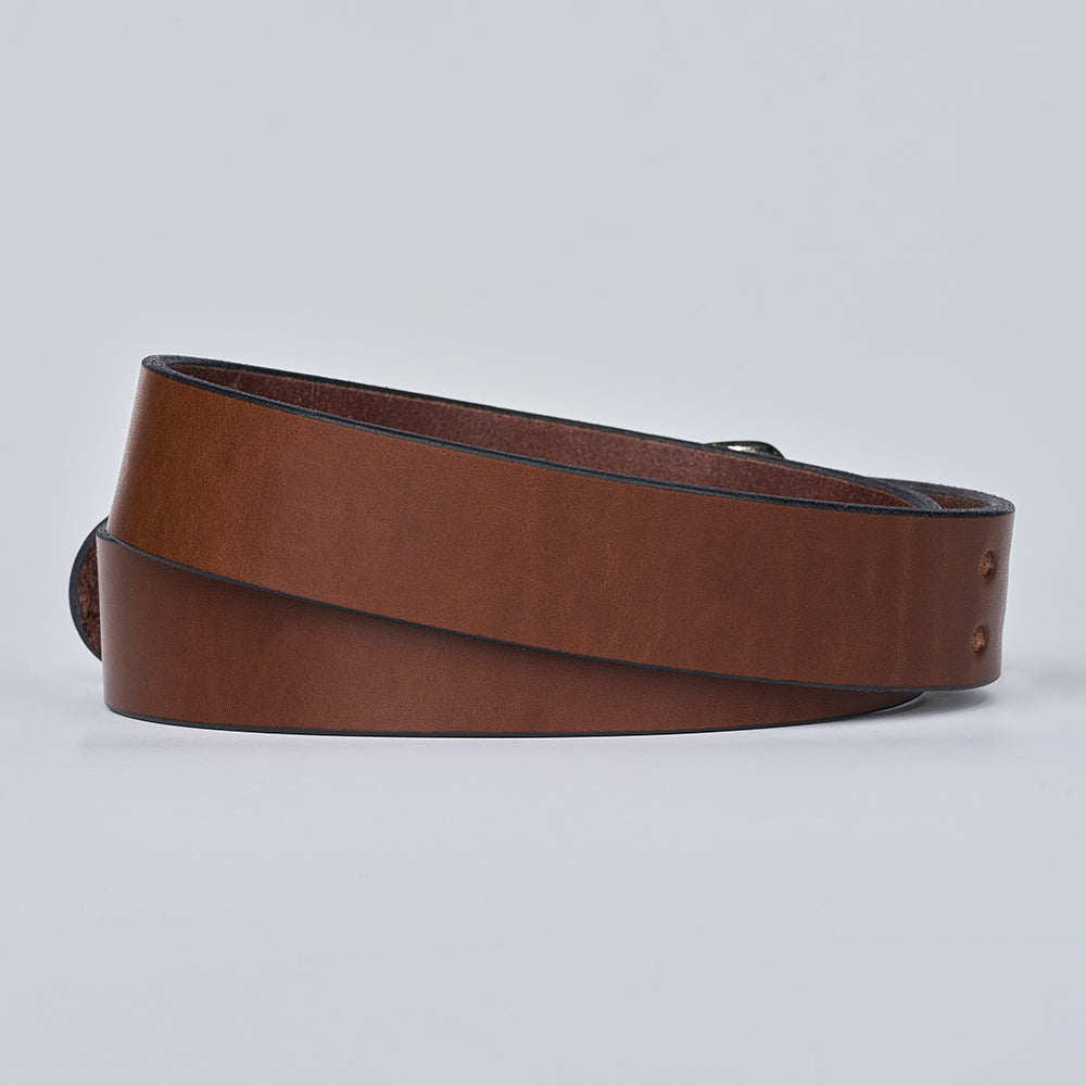 The Double Prong Everyday by Hanks Belts is a coiled brown full-grain leather belt with a subtle sheen and two small rivets near the end, displayed buckle-free against a plain light gray background.