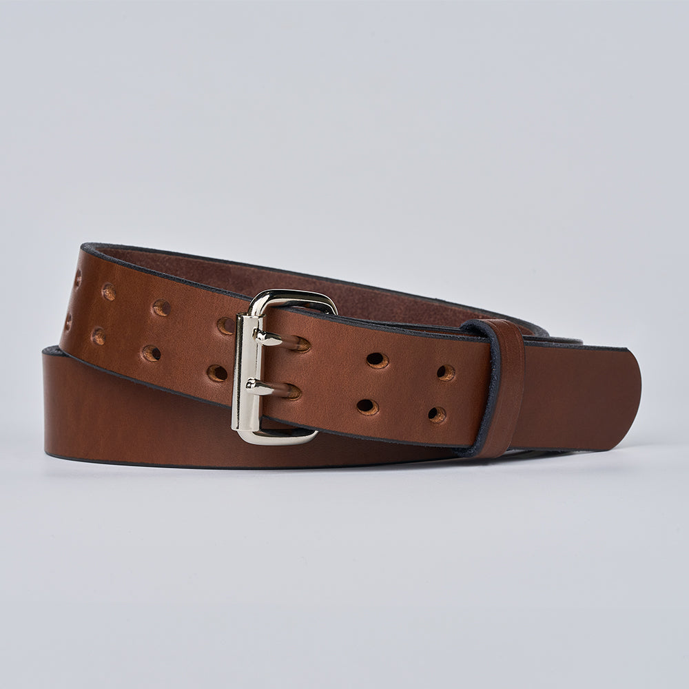 The Double Prong Everyday by Hanks Belts is a brown full-grain leather belt with multiple holes and a silver buckle, coiled on a light gray background—ideal as a classic work belt for daily wear.