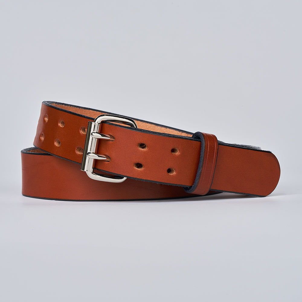 The Double Prong Everyday by Hanks Belts, crafted from brown full-grain leather with a silver buckle, is coiled on a light gray background. Multiple holes enhance its adjustability, making it an ideal sturdy work belt.