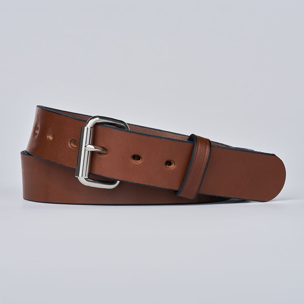 The Gunner by Hanks Belts—a brown leather belt with a silver rectangular buckle, neatly rolled on a light gray background—offers style and durability, making it the ideal CCW belt for any wardrobe.