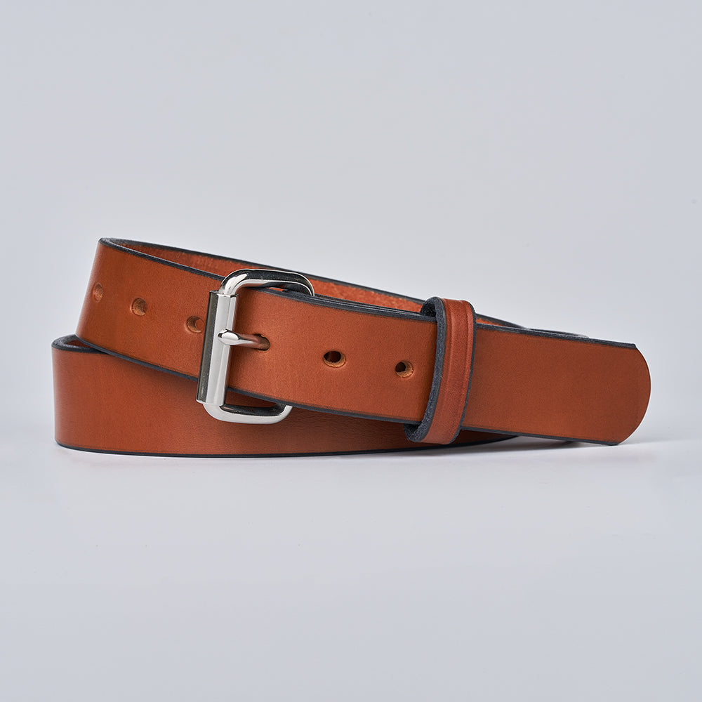 The Gunner by Hanks Belts, a brown leather CCW belt with a silver buckle, is rolled up and displayed on a plain light gray background.
