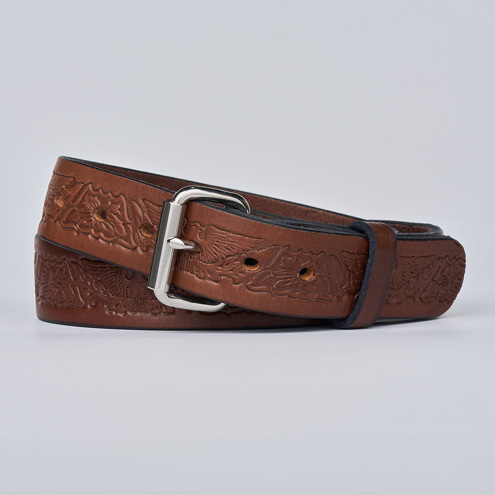 The Gunner Eagle by Hanks Belts, a brown full-grain leather gun belt with an embossed floral pattern, silver buckle, and multiple holes, is neatly coiled on a plain light gray background.