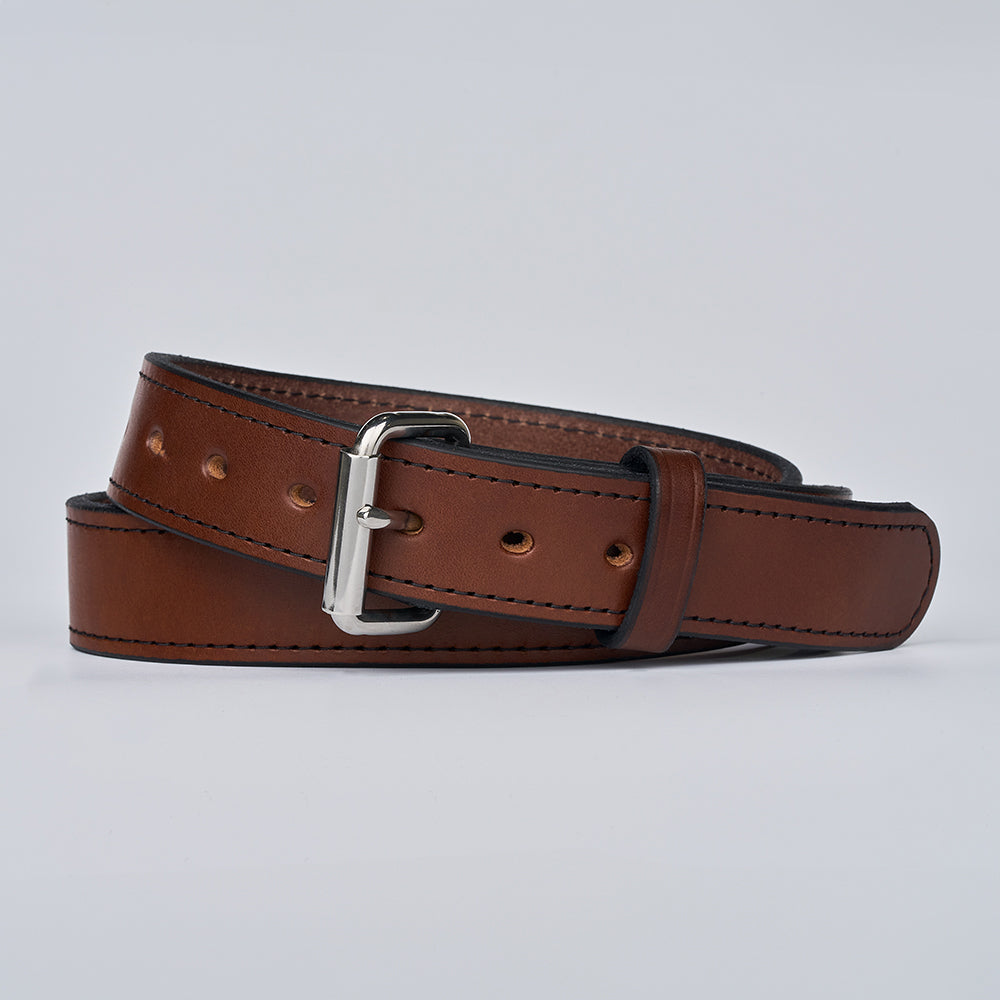 The Gunner Stitched by Hanks Belts is a full-grain leather CCW belt with black stitching, multiple holes, and a silver metal buckle, coiled loosely on a plain light background.