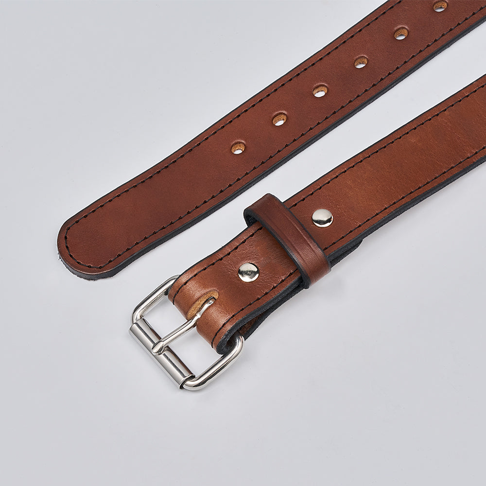 A close-up of The Gunner Stitched full-grain leather belt by Hanks Belts, featuring a silver buckle and multiple adjustment holes, shown on a light gray background.