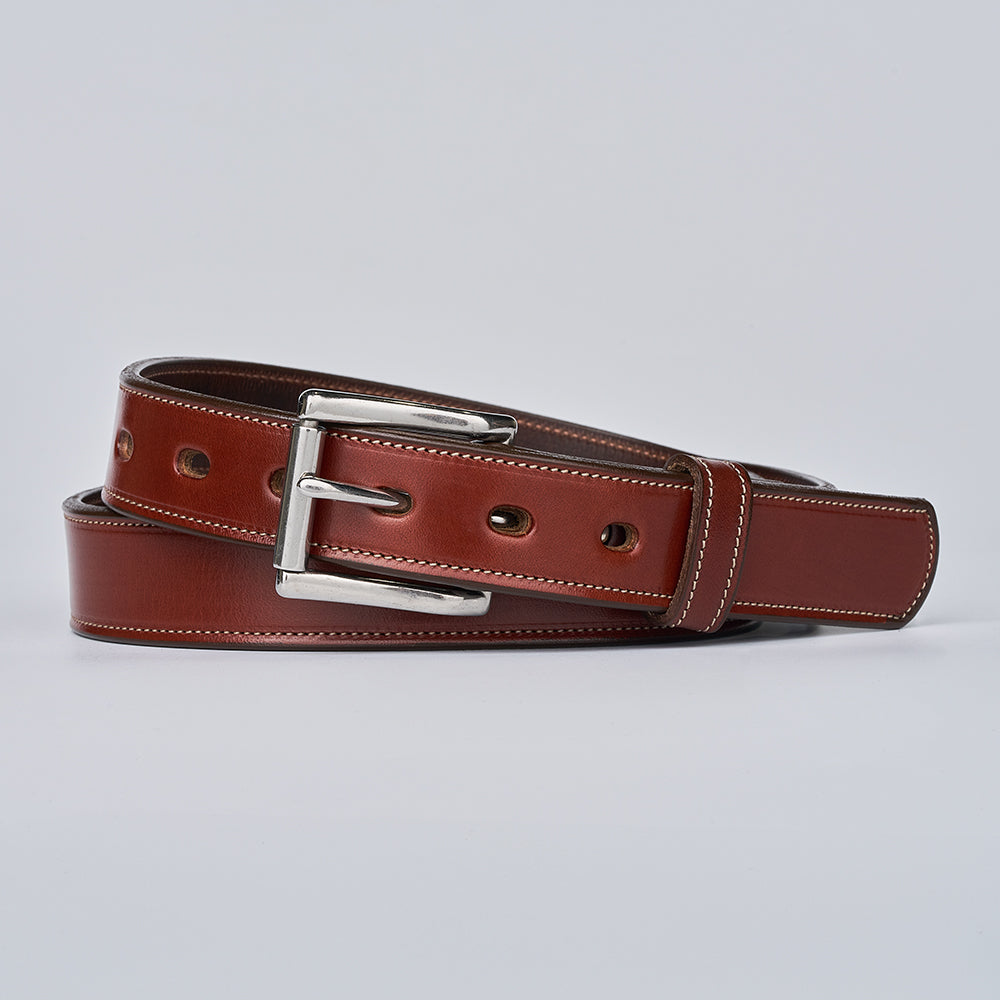 The Highland Lined by Hanks Belts, a brown English bridle leather belt with white stitching and a silver buckle, is coiled neatly against a plain light gray background.