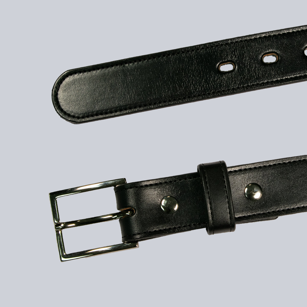 The Ledger by Hanks Belts is a black leather belt with a silver buckle, metallic rivets near the buckle, and multiple adjustment holes, displayed diagonally on a light gray background.
