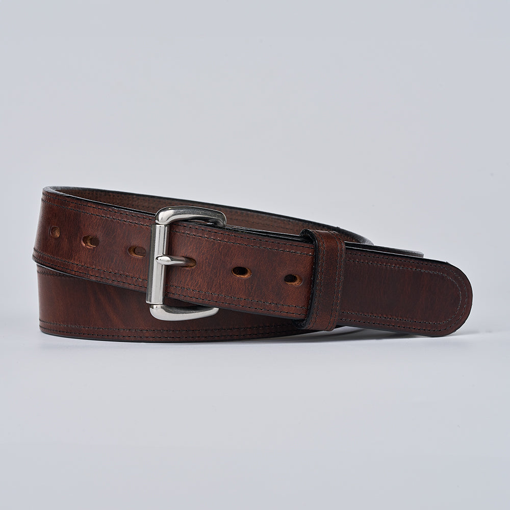 The Old World Harness by Hanks Belts, a full-grain leather belt with a silver rectangular buckle, is shown rolled up against a plain light gray background.