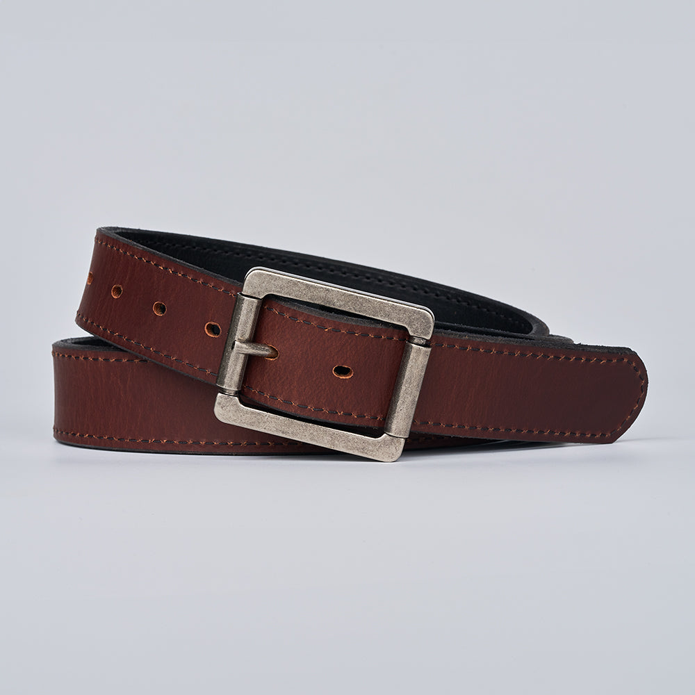 The Reversible by Hanks Belts is a coiled brown leather CCW belt with visible stitching and a silver rectangular buckle, displayed on a plain light gray background.