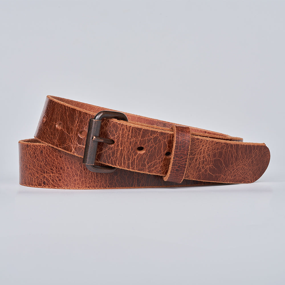 The Rustic Glazed by Hanks Belts is a textured leather belt with a dark metal buckle, elegantly coiled on a light gray background.
