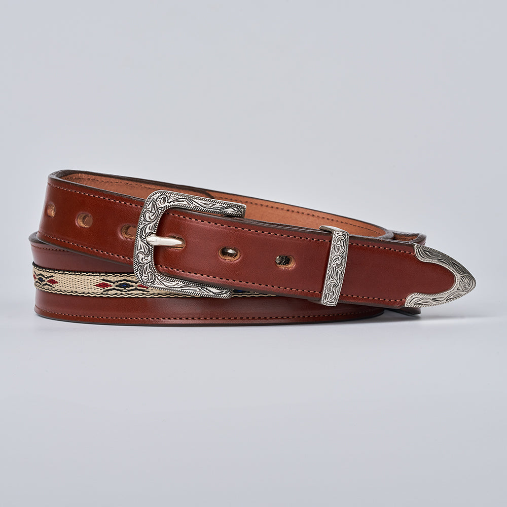 The Seneca Tapered by Hanks Belts features a brown English bridle leather strap, ornate silver buckle and tip, Aztec-inspired beige woven accent with red and black details, and decorative embossing, shown coiled on a plain light background.