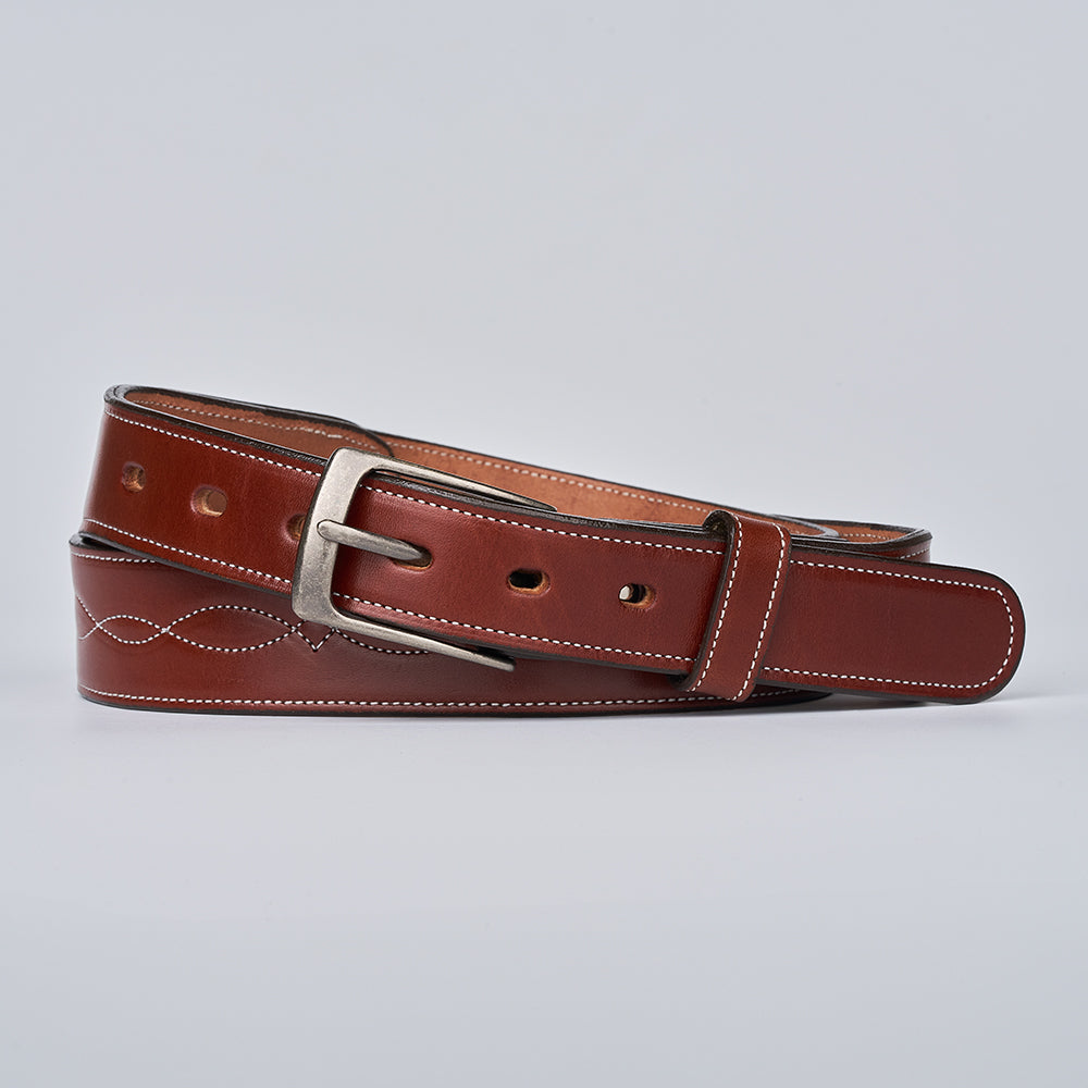 The Teton Tapered by Hanks Belts is a handcrafted English bridle leather belt with white stitching, a silver buckle, and decorative perforations, shown rolled up on a plain light gray background.