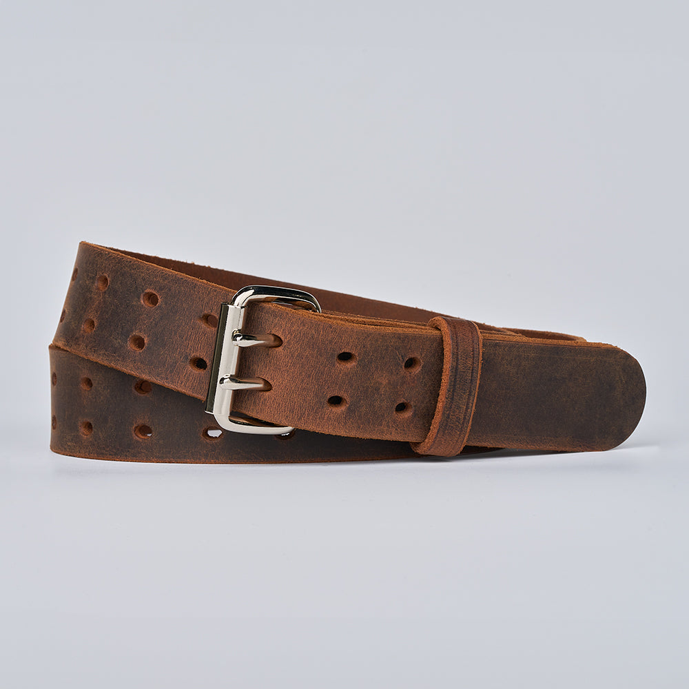 The Woodstock Double Prong Retro Style full-grain leather belt by Hanks Belts, featuring multiple holes and a silver buckle, is coiled on a plain light gray background.