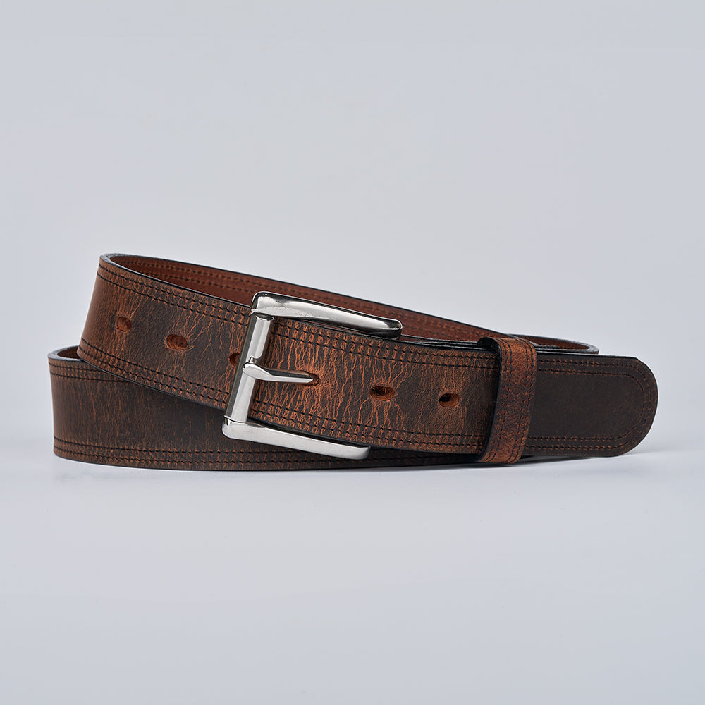 The Wyoming Bison belt by Hanks Belts, made from brown bison leather with a silver buckle, is coiled and displayed against a plain light gray background.