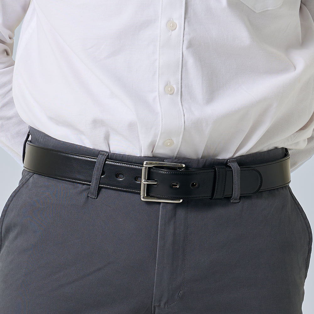 A person wearing a white button-up shirt tucked into gray pants, showcasing The Canyon belt by Hanks Belts, handcrafted from vegetable-tanned leather with a silver buckle. The image highlights the waist and midsection.